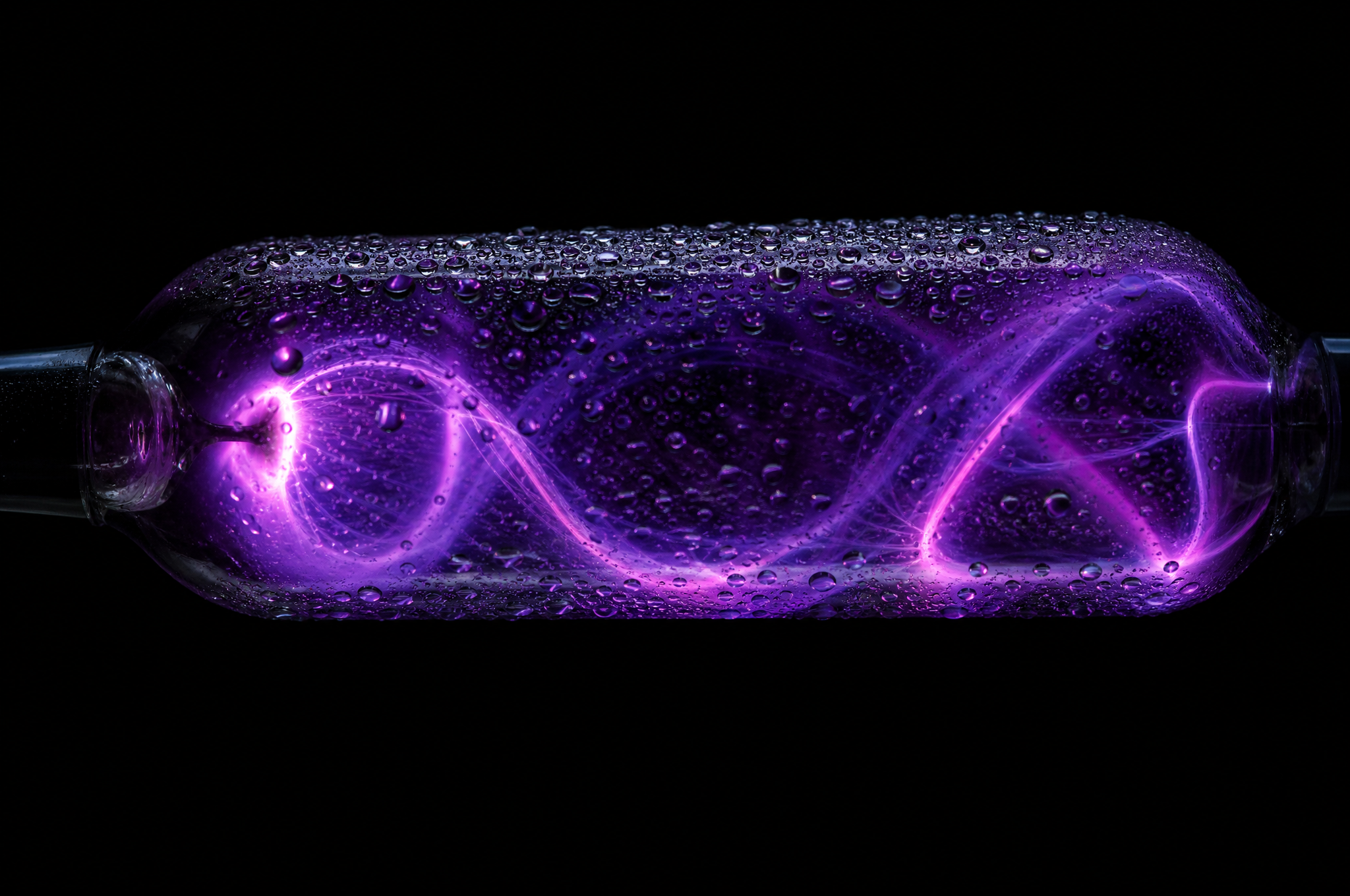 Close view of a plasma discharge tube, ribbons of violet and magenta light coiling inside condensation-covered glass against a black background.