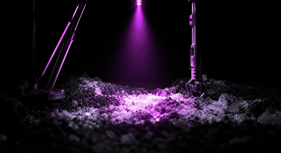 A single violet lamp beam from a lunar hopping probe lights a patch of icy regolith inside a crater otherwise in total darkness.