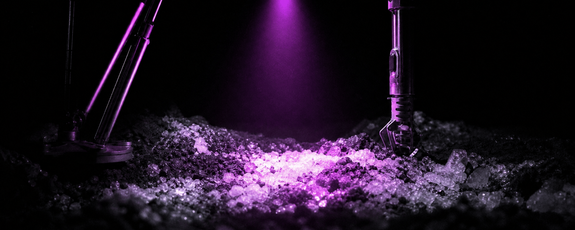 A single violet lamp beam from a lunar hopping probe lights a patch of icy regolith inside a crater otherwise in total darkness.
