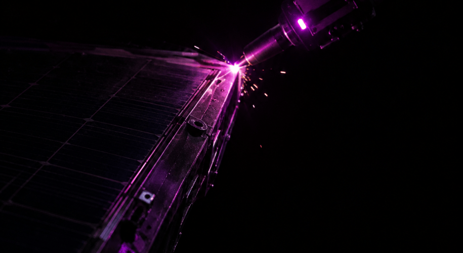 A robotic arm fitted with a compact electron-beam welding tool repairs the hull of a damaged satellite, backlit by low golden sunlight with Earth visible below.