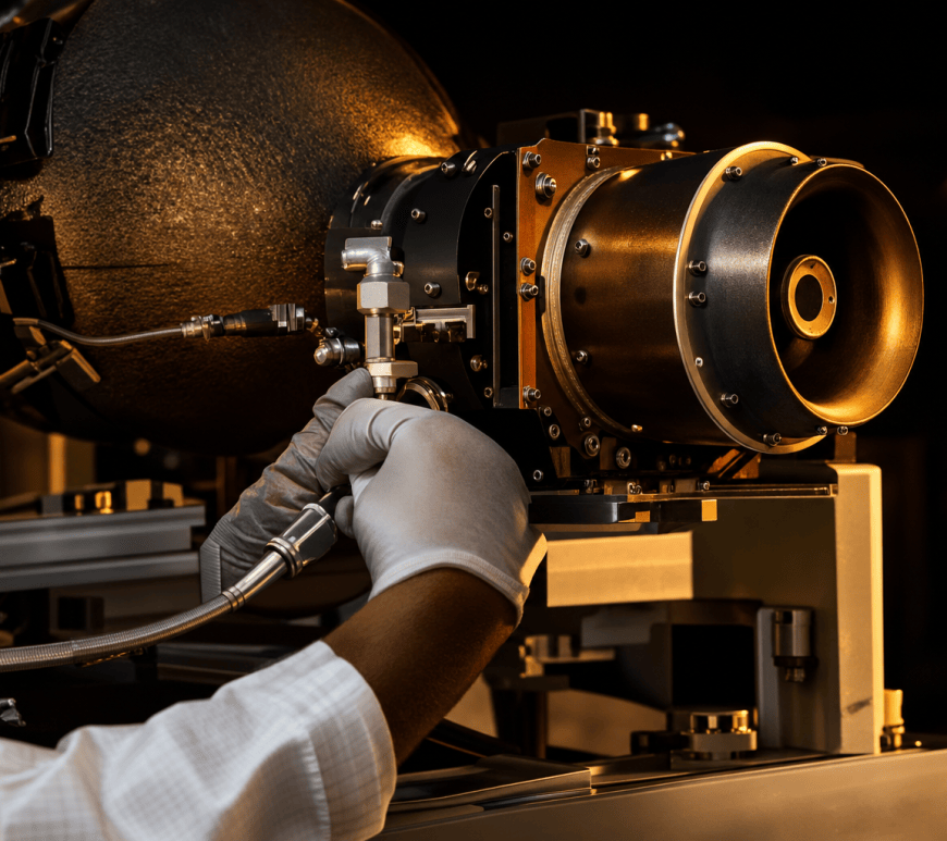 A technician's gloved hand steadies a xenon feed line on a satellite Hall-effect thruster mounted on an assembly stand, under raking golden light.